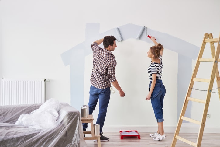A man and woman painting a wall in their home.